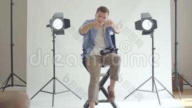 专业的男<strong>摄影</strong>师坐在椅子上，用手指注视着<strong>摄影</strong>棚里的<strong>摄像</strong>机。